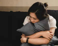 Sad woman sitting on couch hugging a pillow